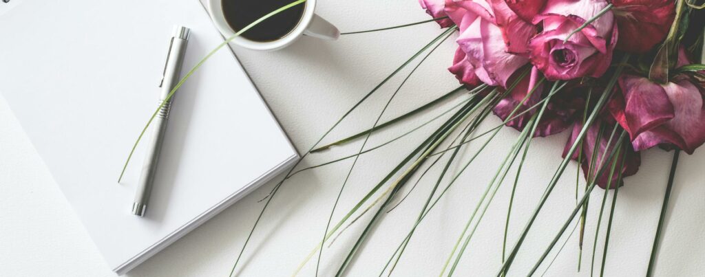 red rose flowers bouquet on white surface beside spring book with click pen and cup of cofffee